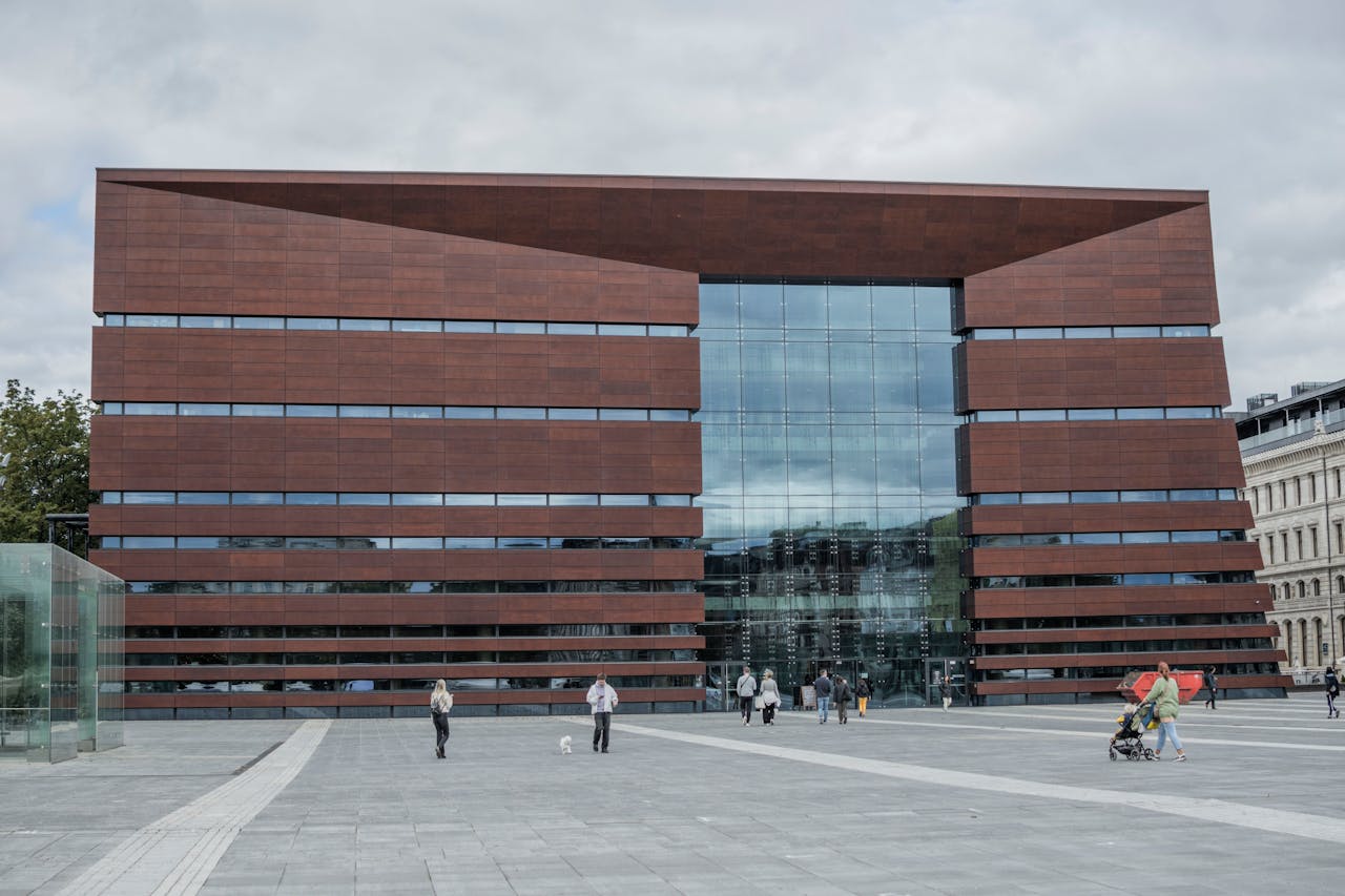 Nowoczesny gmach Narodowego Forum Muzyki we Wrocławiu z czerwonej bryły i przeszkloną fasadą, widziany z szerokiego placu, po którym spacerują mieszkańcy – symbol kosztownej, ale ważnej inwestycji kulturalnej miasta.